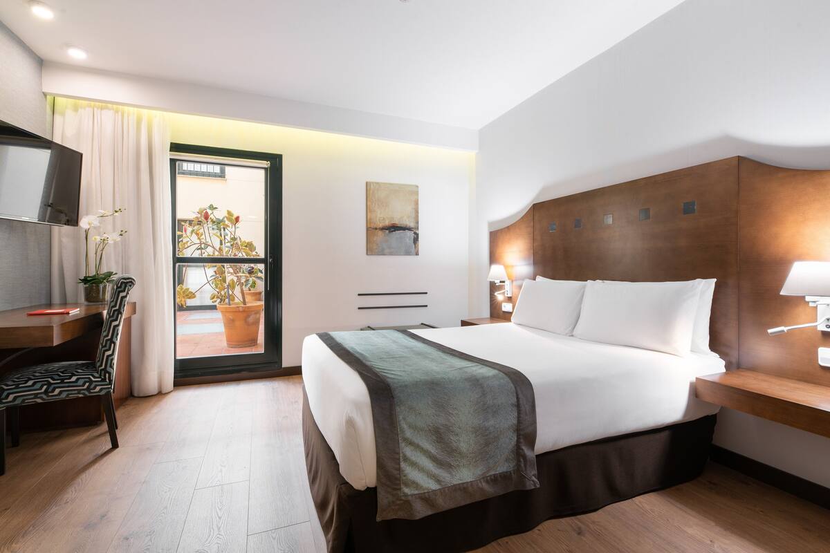 A modern hotel room with a large bed, a desk, a chair, and a TV.