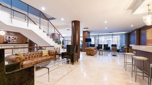 A spacious lobby with a high ceiling, a staircase, leather sofas, and a bar area. - Dorma Ágora Caceres (Cáceres)