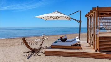 Un entorno playero con una hamaca, sillas de descanso y una terraza de madera.