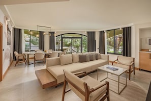 Amplia sala de estar con sofá, sillones, una mesa de centro y una mesa de comedor. Ventanas grandes ofrecen vistas al exterior.