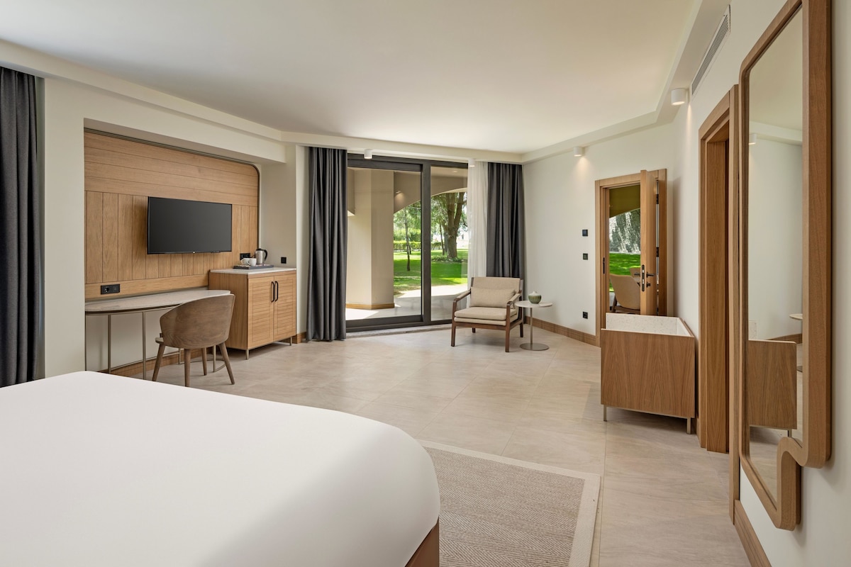 Een moderne hotelkamer met een groot bed, een bureau met stoel, een televisie, een bijzettafeltje met stoel en een badkamer met spiegel.