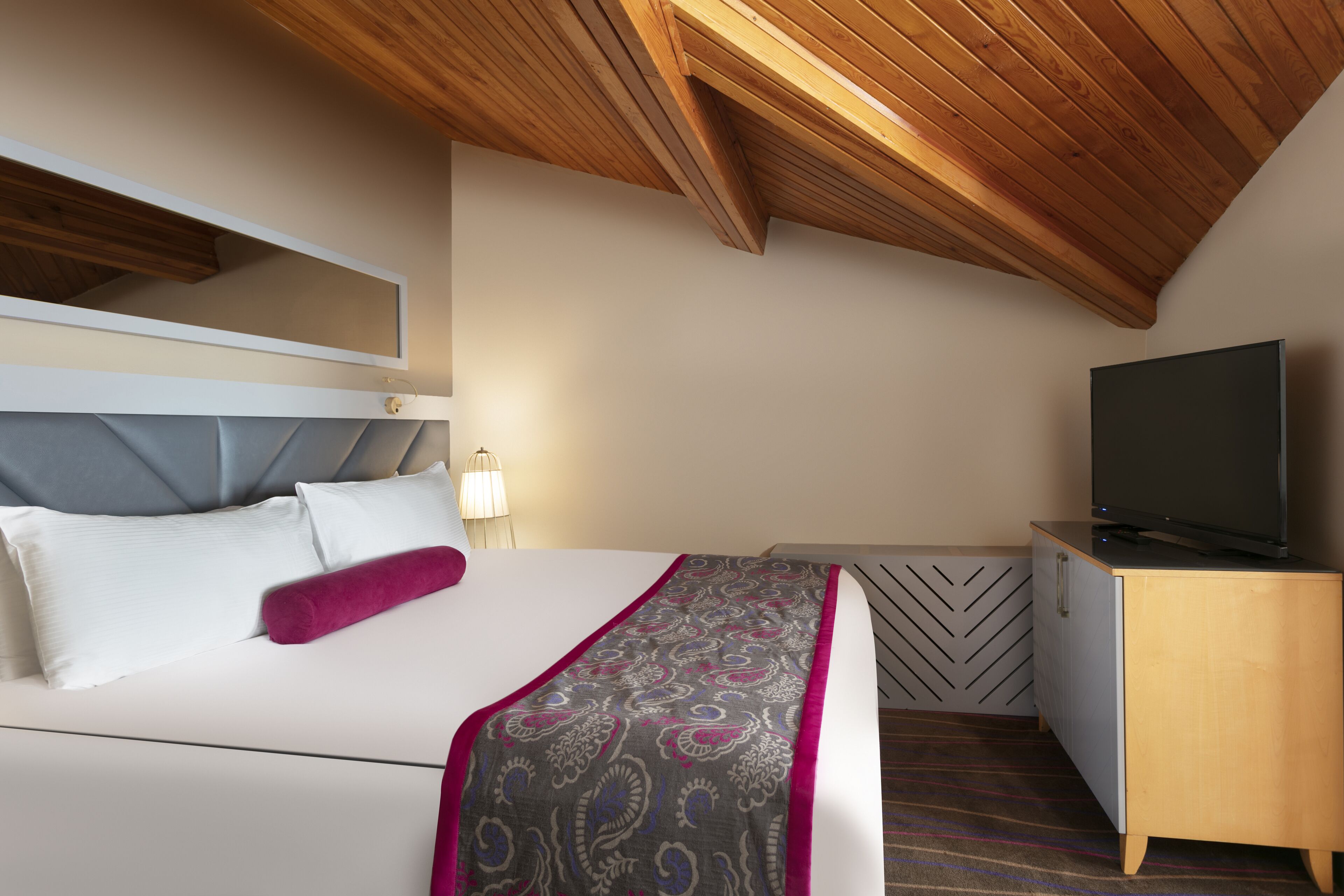 Una habitación de hotel con una cama, un televisor, techo de madera y un mueble con motivo de espiga.