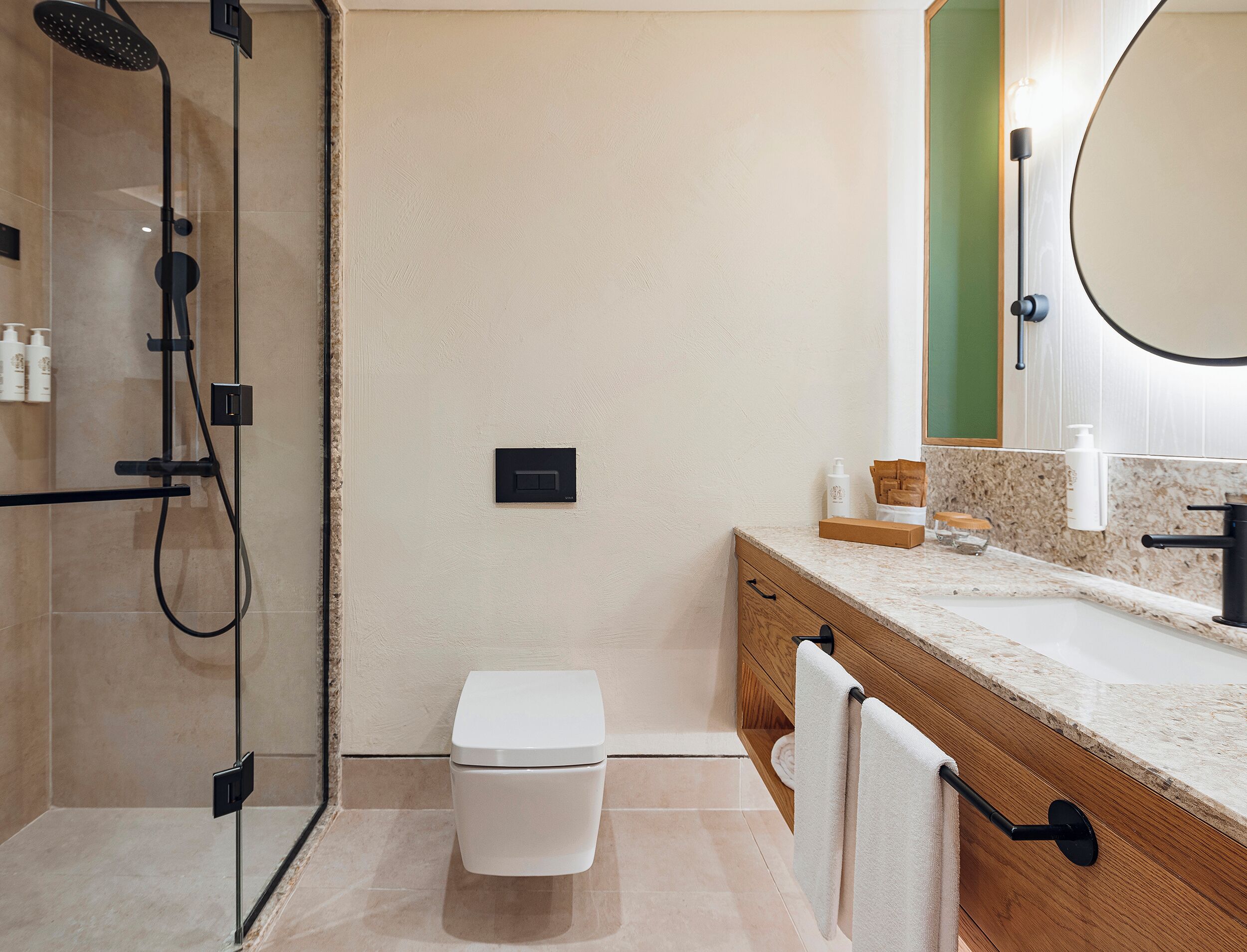 Un baño moderno con ducha envuelta en vidrio, inodoro, tocador con encimera de mármol y espejo.