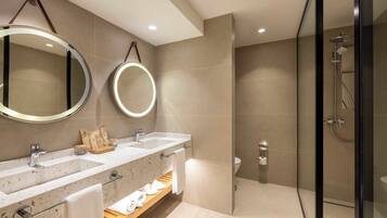 A modern bathroom with two sinks, a glass shower enclosure, and a mirror with a light.