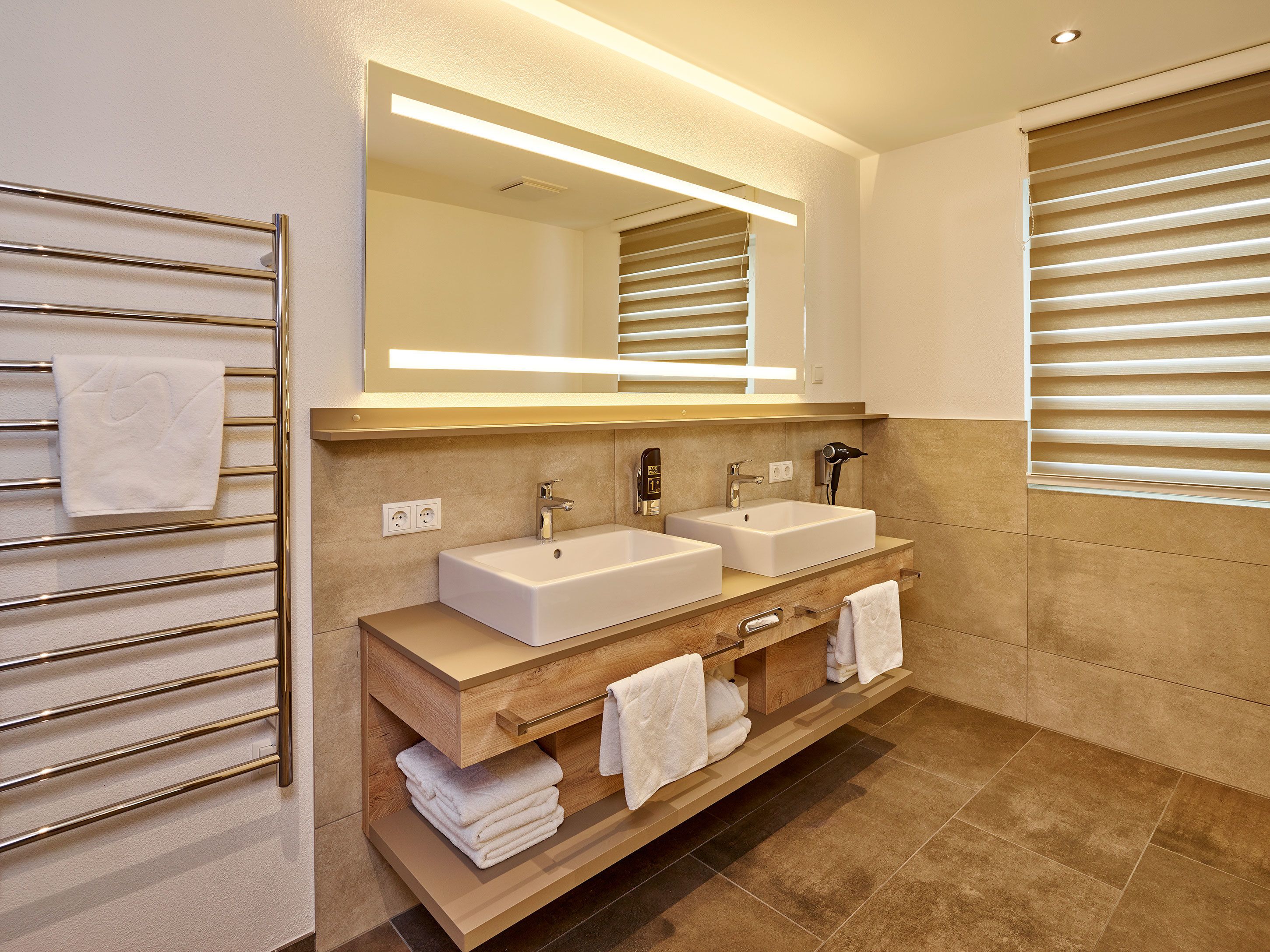 Ein modernes Badezimmer mit zwei Waschbecken, einem großen Spiegel und einem Handtuchhalter.