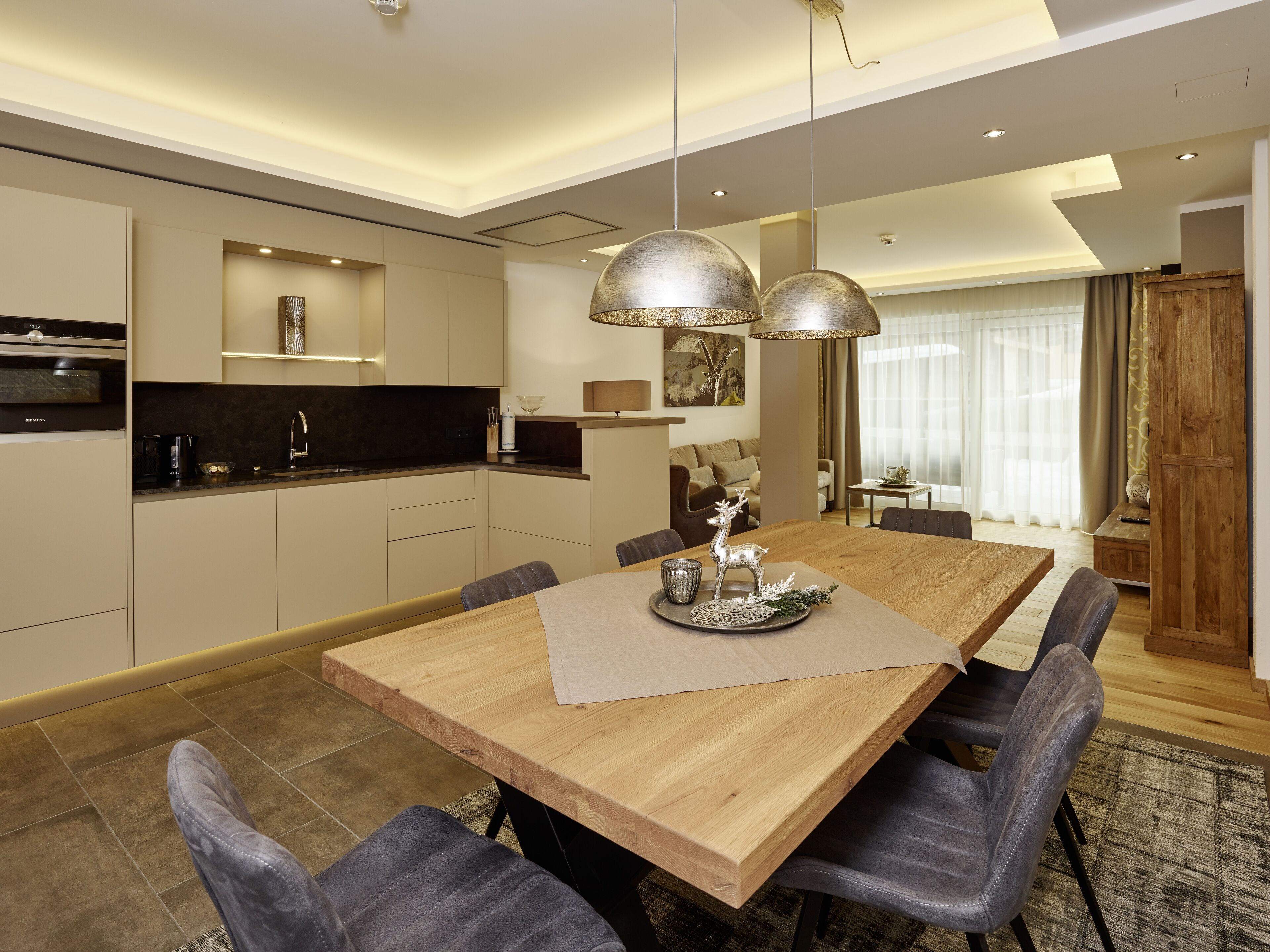 Una cocina moderna con electrodomésticos integrados, un comedor con mesa y sillas de madera, e iluminación colgante.