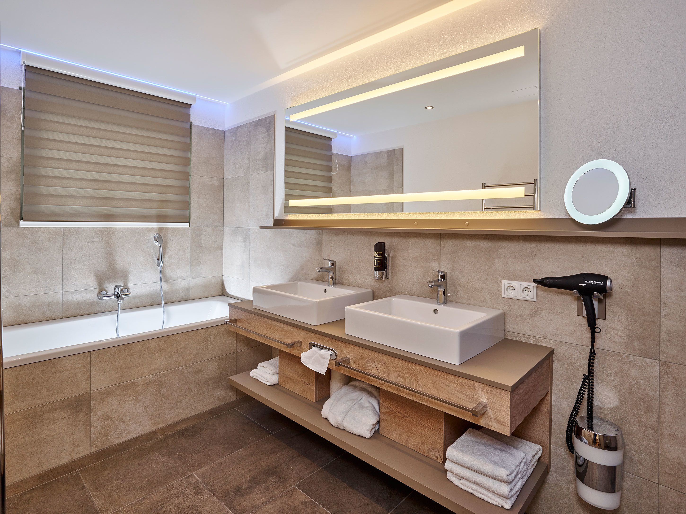 Een moderne badkamer met een badkuip, twee wastafels, een wastafelmeubel met spiegel en een haardroger.