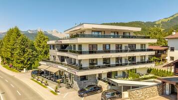 A multi-story hotel with a restaurant on the ground floor, outdoor seating, and a view of mountains.