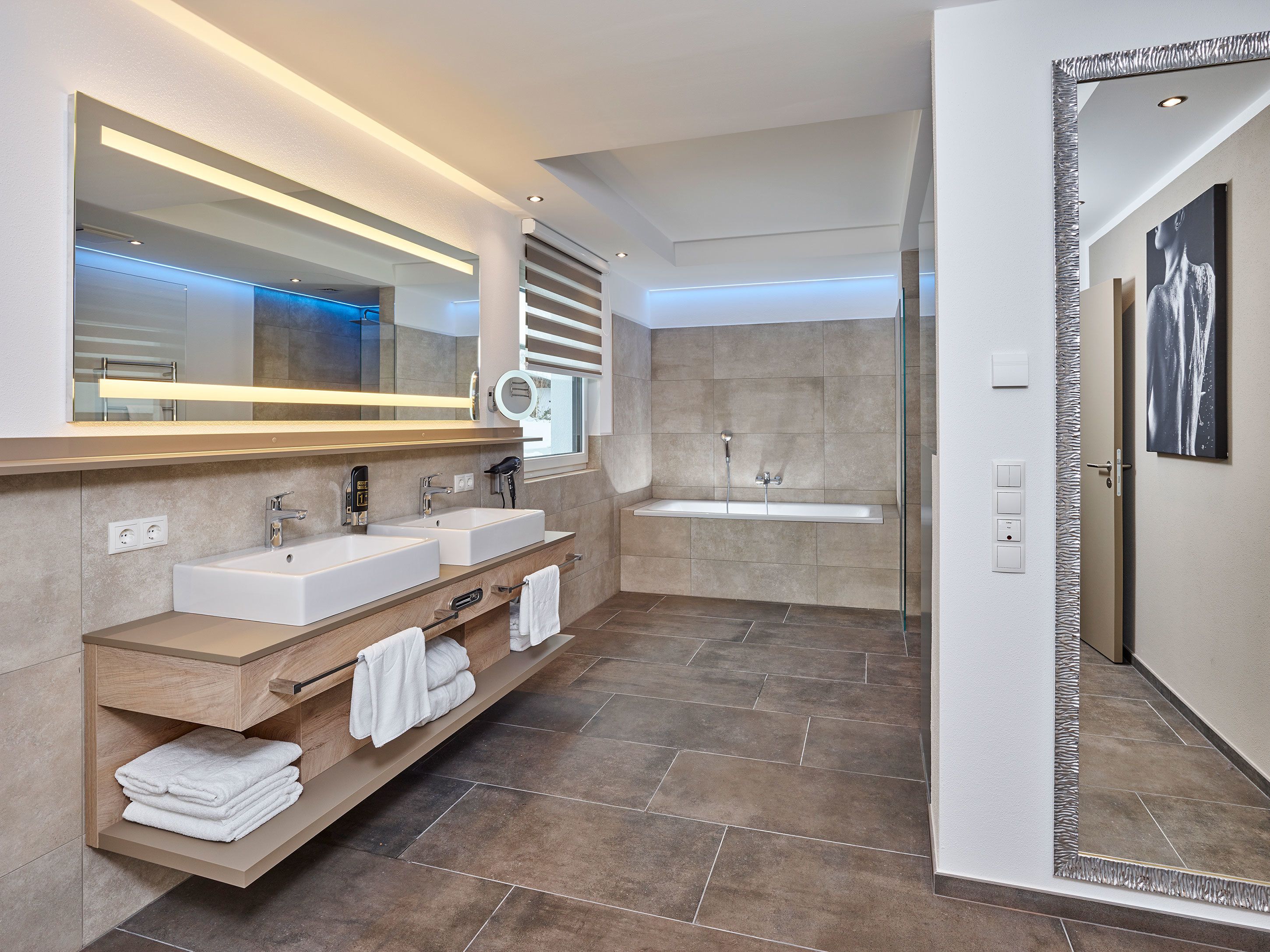 Un baño moderno con dos lavamanos, un espejo grande y una bañera.