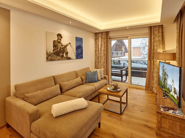 A living room with a sofa, a coffee table, a flat-screen TV, and a painting on the wall. - A-VITA Living Luxury Appartements (Seefeld in Tirol)