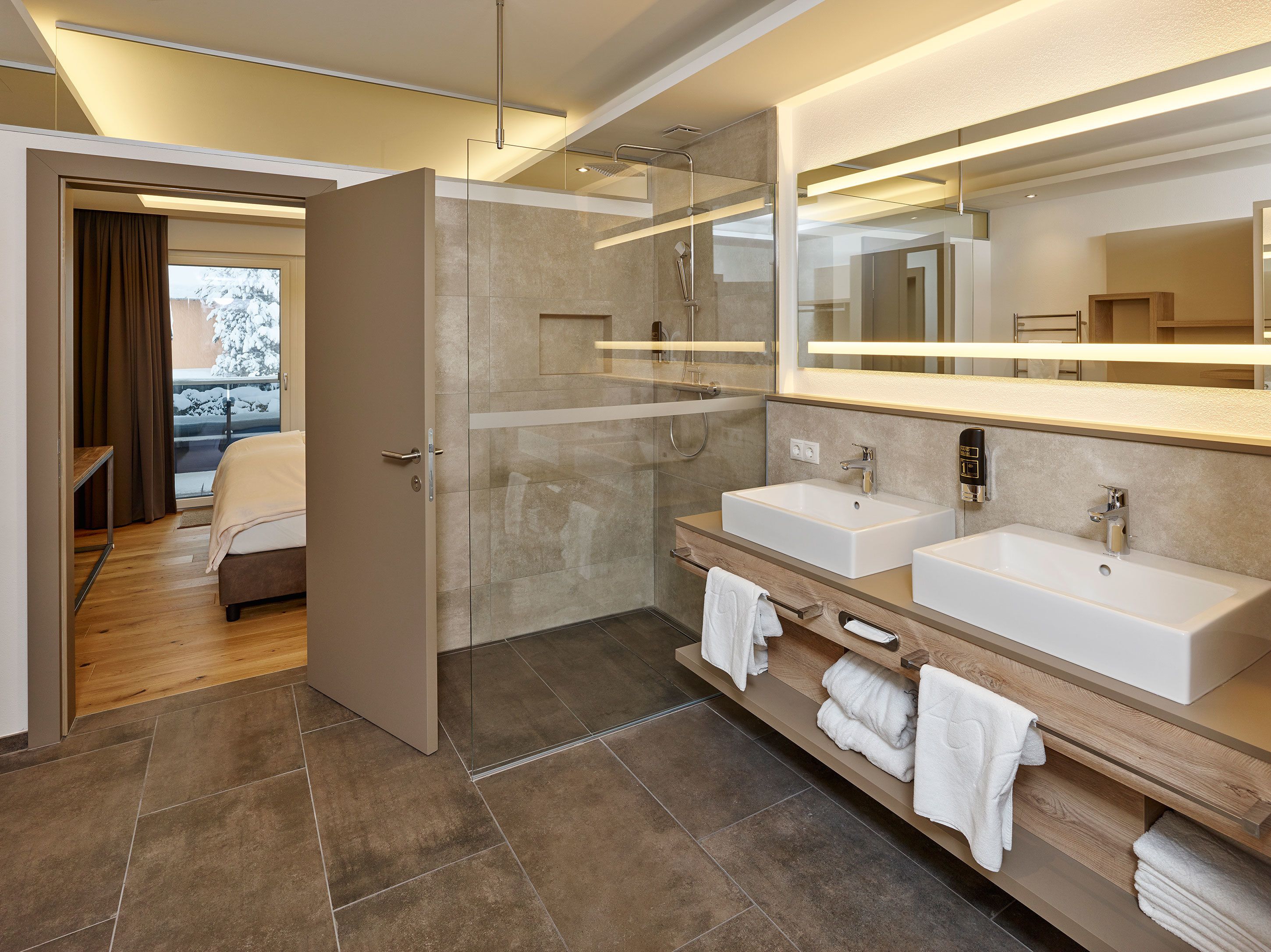 A modern bathroom with two sinks, a large mirror, and a shower area.