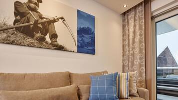 A living room with a beige sofa, a blue and white pillow, and a painting of a person fishing.