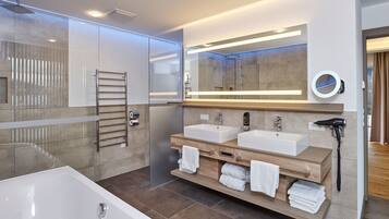 A modern bathroom with a large bathtub, two sinks, a towel rack, and a mirror with a built-in phone.