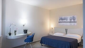Una camera da letto con un letto, una scrivania con una sedia, una lampada a parete e un quadro.