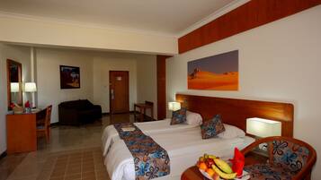 Habitación de hotel con dos camas, un escritorio, una silla y una mesa de comedor con fruta.