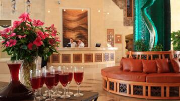 Un área de recepción con una mesa de recepción, un jarrón de flores y varias copas de vino tinto sobre una mesa.