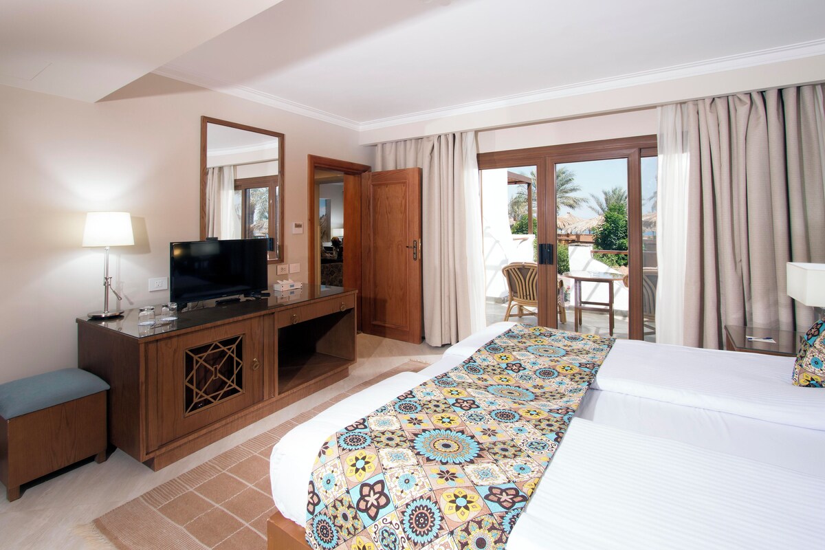 A hotel room with a bed, a television, a desk, and a balcony with a chair.