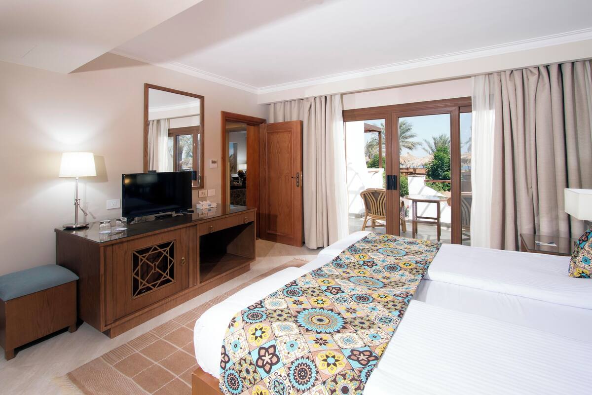 A hotel room with a bed, a television, a desk, and a balcony with a chair.