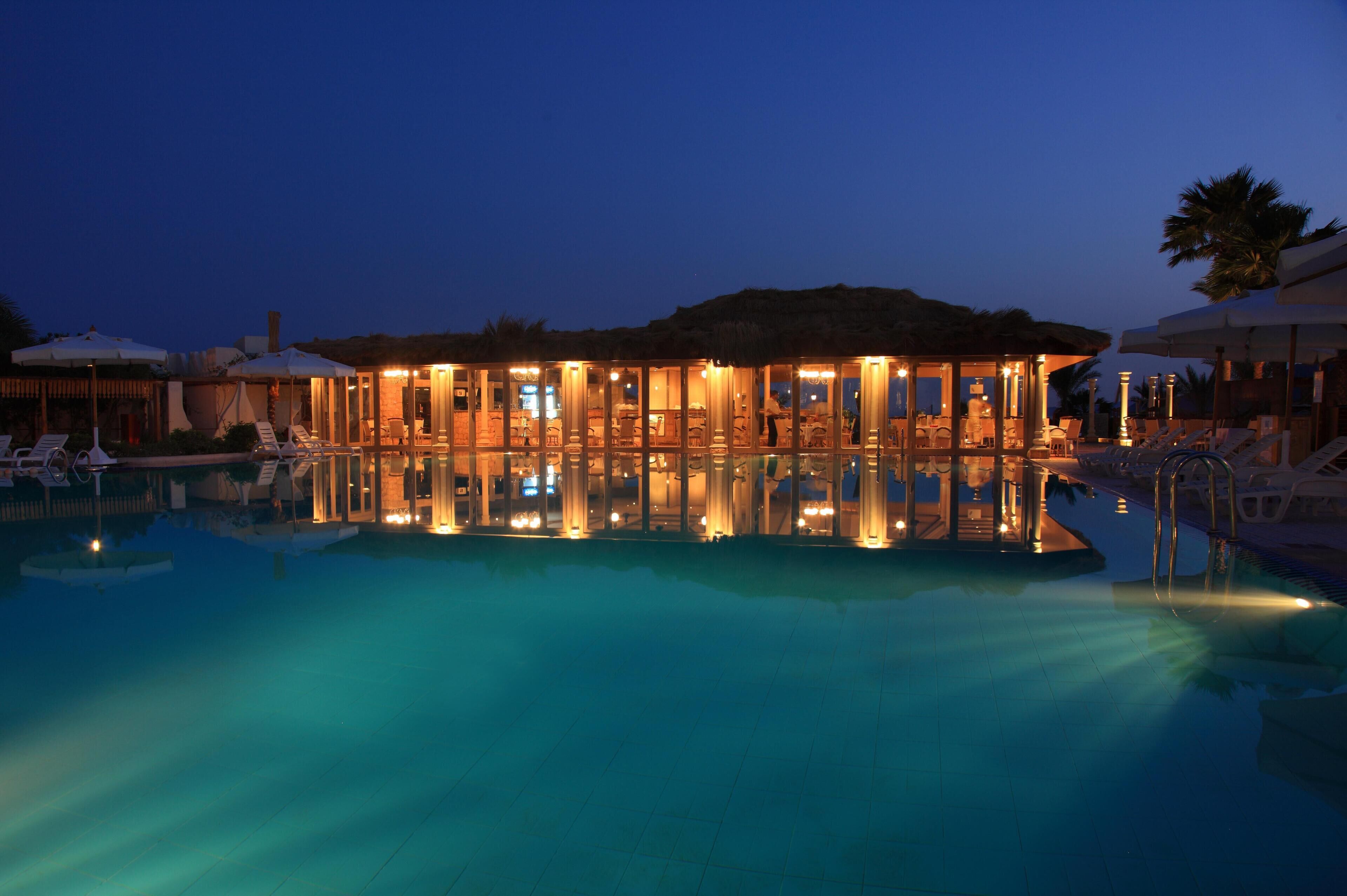 Un hotel con piscina, sillas de descanso y sombrillas.