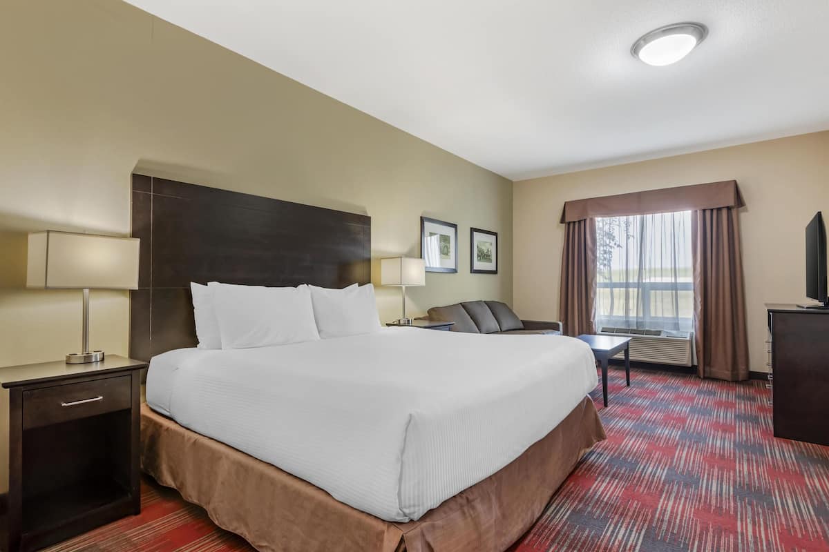 A hotel room with a large bed, bedside tables, a desk, and a window with curtains.