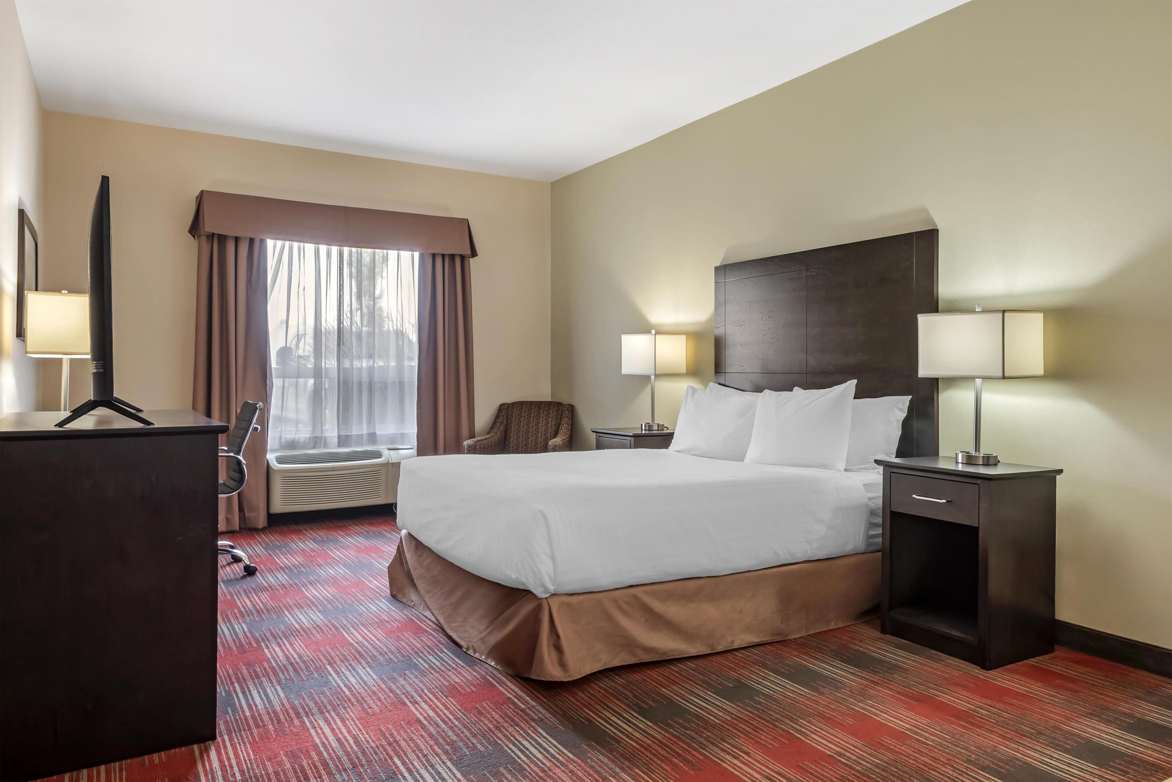 Une chambre d’hôtel avec un grand lit, deux tables de chevet avec des lampes, un bureau, une chaise et une fenêtre avec des rideaux.