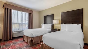A hotel room with two beds, a window with curtains, a bedside table with a lamp, and a red carpet.