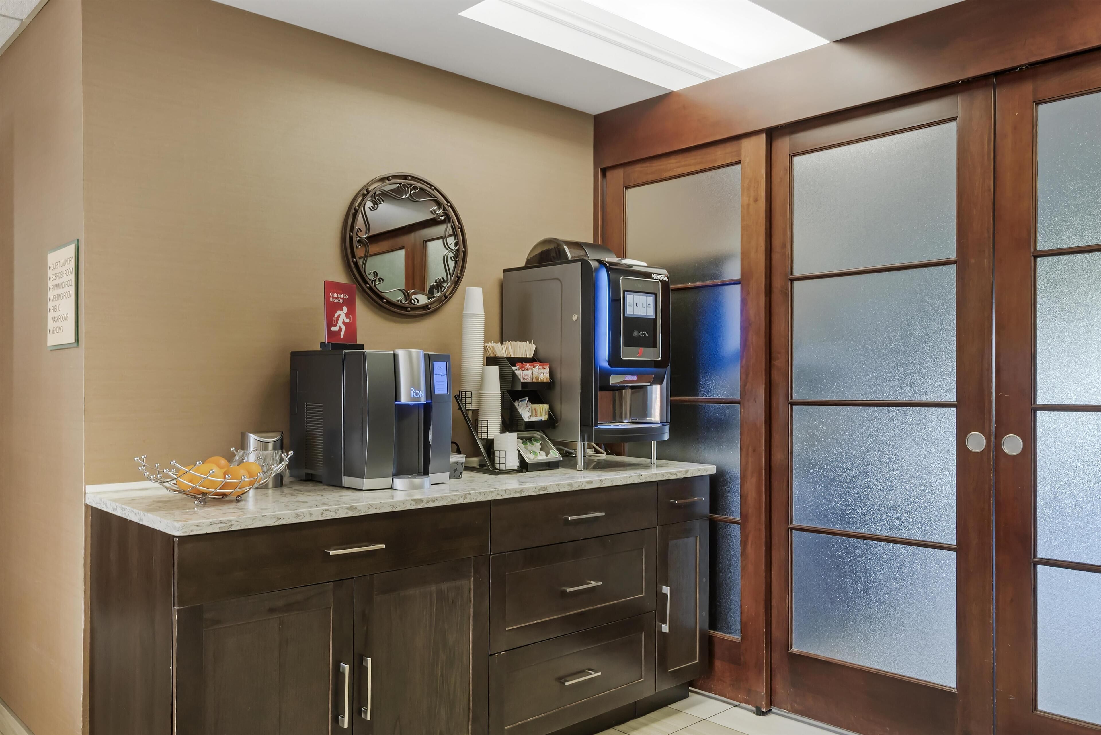 A hotel reception area with a coffee machine, a mirror, and a counter with a basket of oranges.