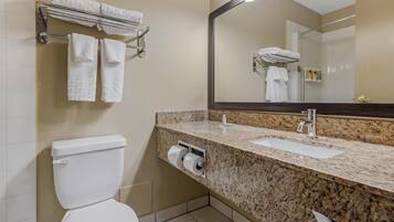 A bathroom with a white toilet, a granite sink, a mirror, and a towel rack with multiple towels.