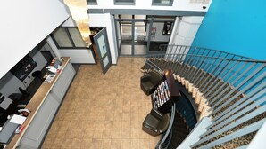 Un vestíbulo de hotel con una recepción, una escalera con alfombra estampada y una pared azul.
