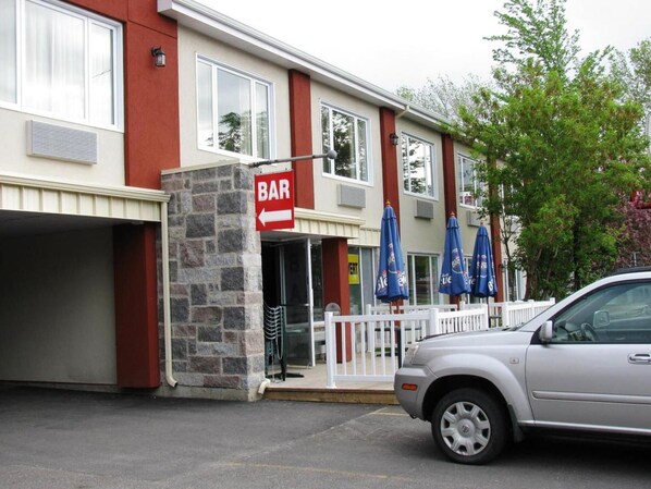Un edificio con un letrero de 'BAR', un pilar de piedra y un coche estacionado.