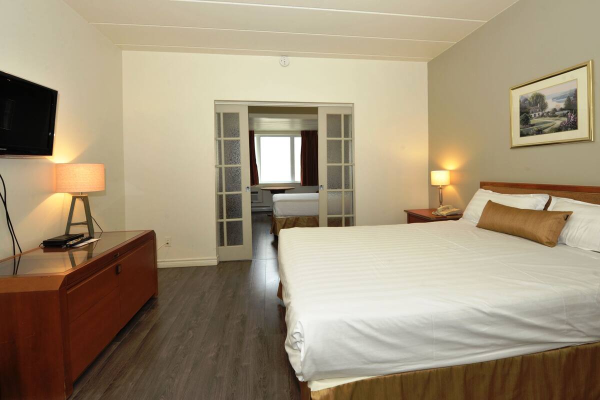 A hotel room with a large bed, a desk with a lamp, a television, and a painting on the wall.