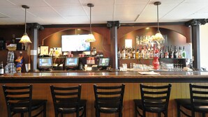 Un bar con una barra larga, múltiples monitores y una gran variedad de botellas y vasos.