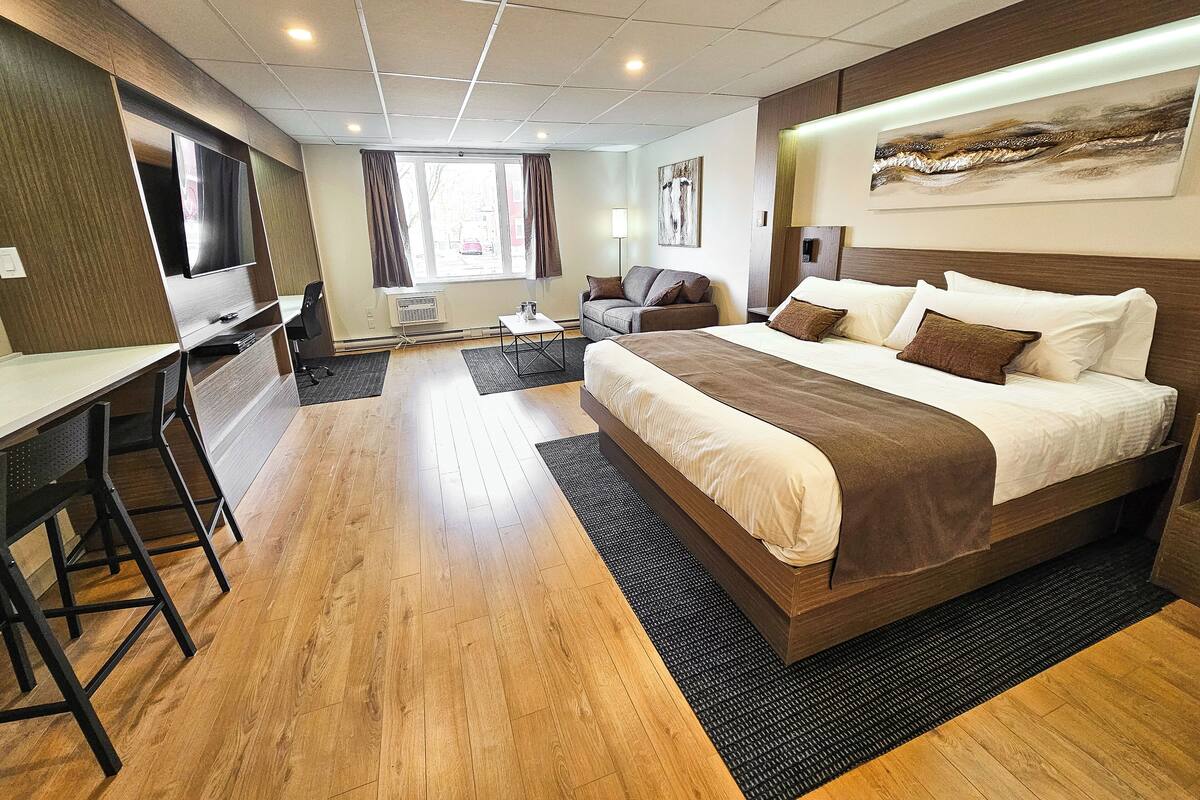 A modern hotel room with a large bed, a desk, a chair, and a TV.
