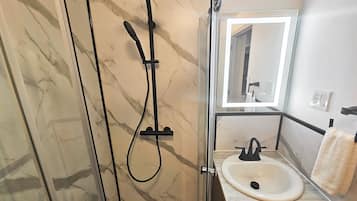 A bathroom with a glass-enclosed shower, a white sink, and a mirror above the sink.