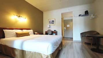 Habitación de hotel con una cama grande, mesita de noche, lámpara y una pequeña zona de estar con una silla y una mesa.