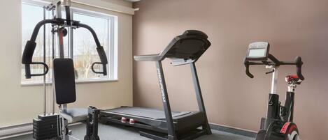 Un gimnasio con cinta de correr, bicicleta estática y equipamiento de levantamiento de pesas.