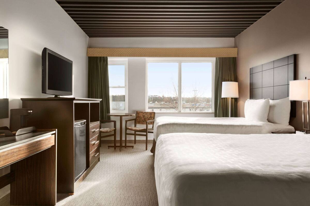 Ein Hotelzimmer mit zwei Betten, einem Schreibtisch mit Fernseher, einem kleinen Tisch und einem Stuhl.