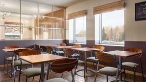 Un comedor con mesas y sillas, ventanas amplias con persianas y vistas al exterior.