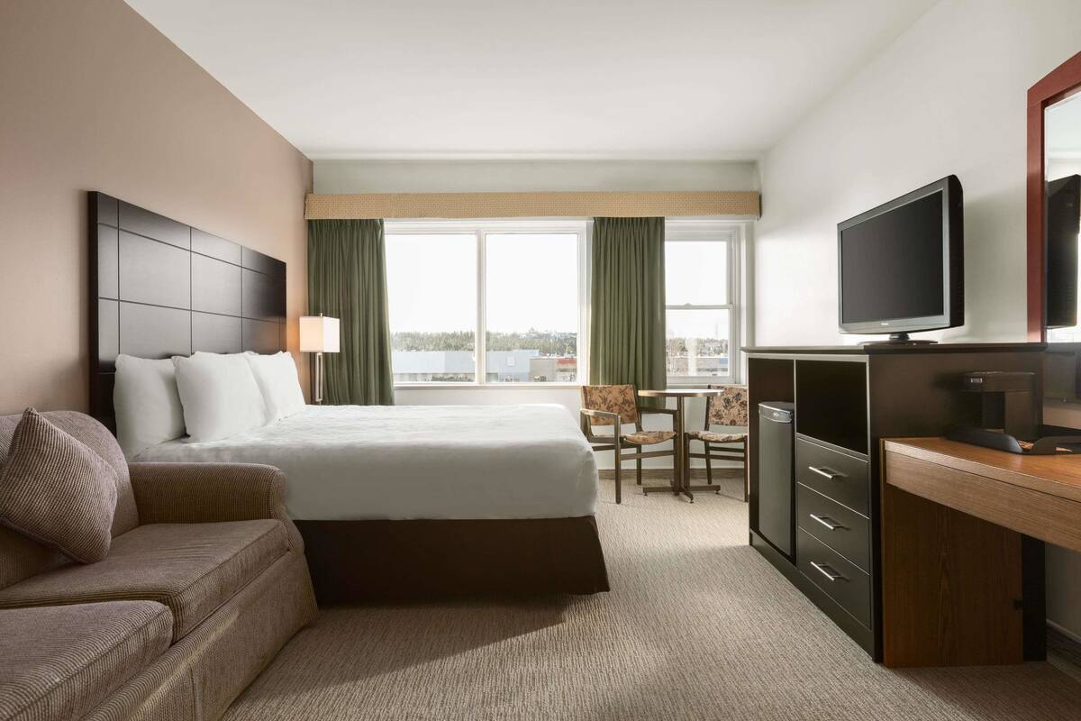 Ein Hotelzimmer mit Bett, Schreibtisch, Fernseher und Blick auf die Stadt.