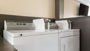 Una lavadora y secadora de carga frontal con un panel de control, un televisor montado en la pared y un dispensador de toallas.