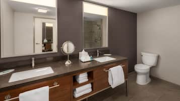 A modern bathroom with a double sink vanity, a large mirror, a toilet, and a shower area.