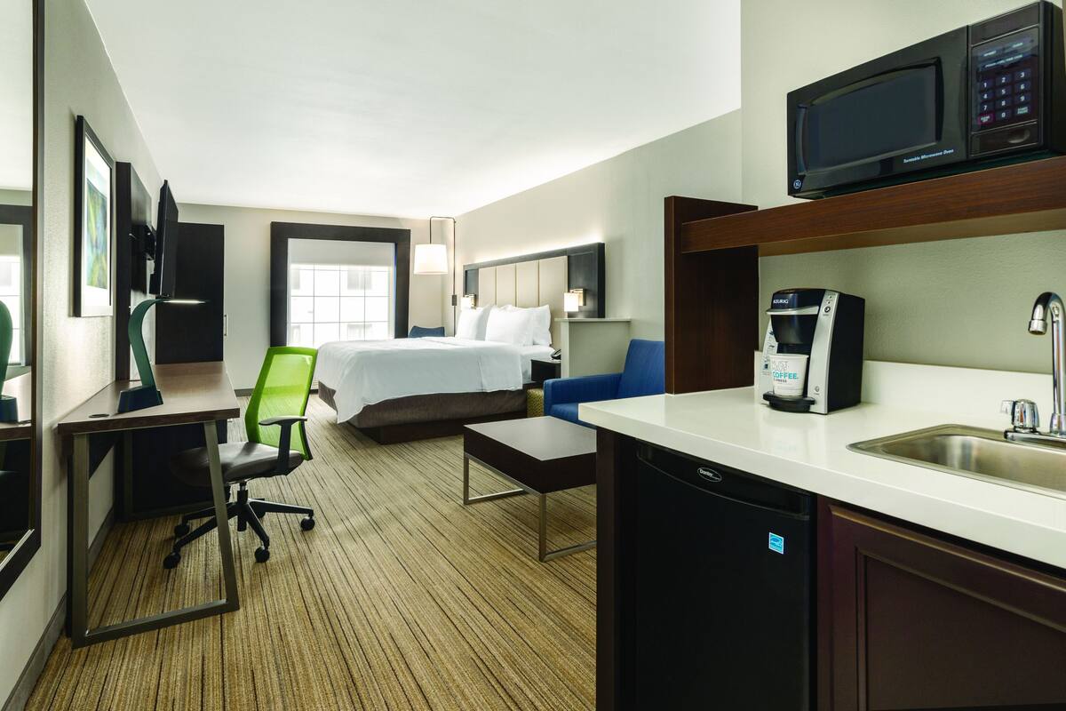 Ein Hotelzimmer mit einem Bett, einem Schreibtisch mit Computer, einem Stuhl, einer Kaffeemaschine und einer Mikrowelle.