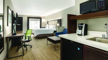 A hotel room with a bed, a desk with a computer, a chair, a coffee machine, and a microwave.