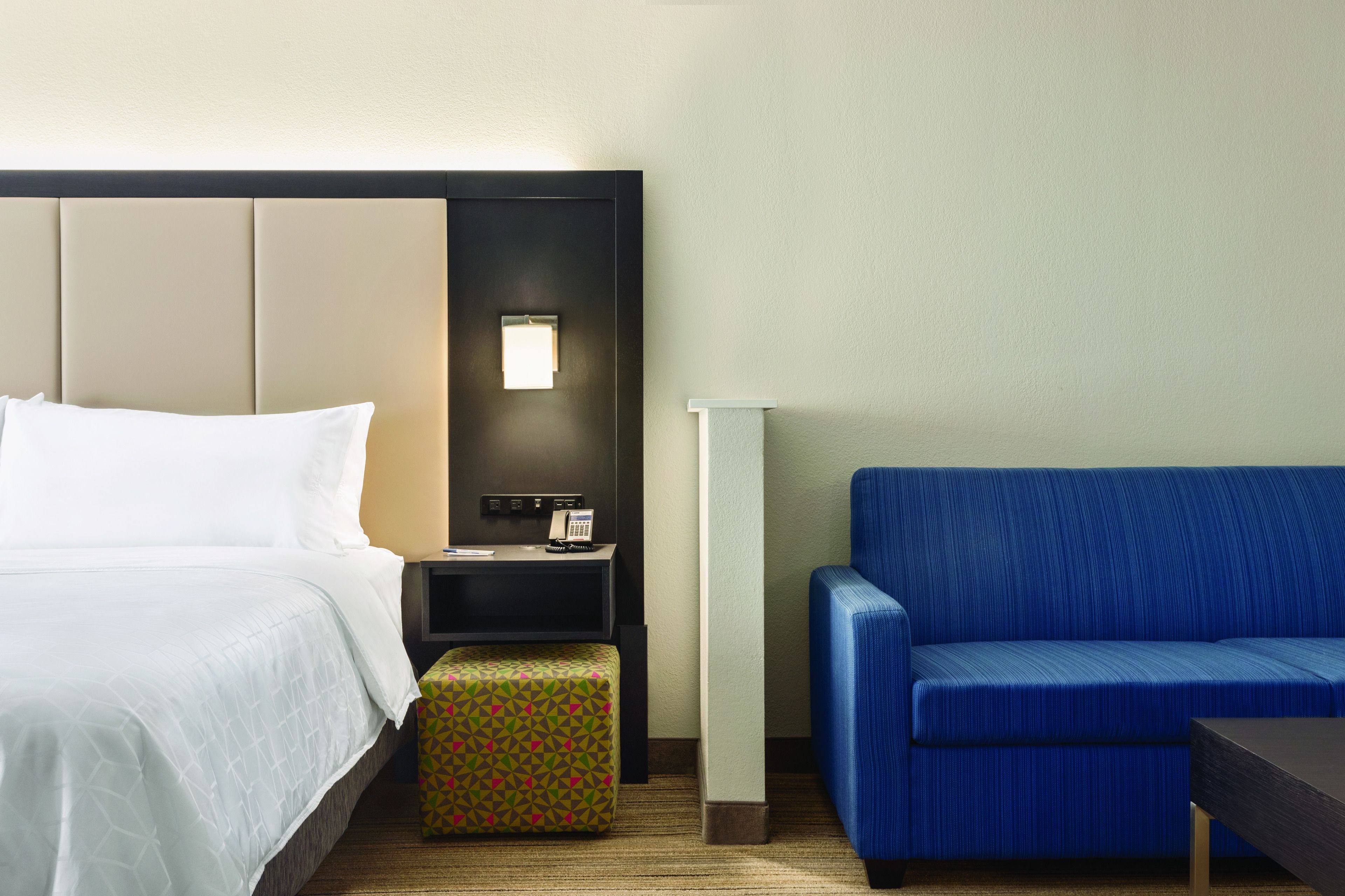 Een hotelkamer met een bed, een nachtkastje, een blauwe bank en een gestreept voetenbankje.