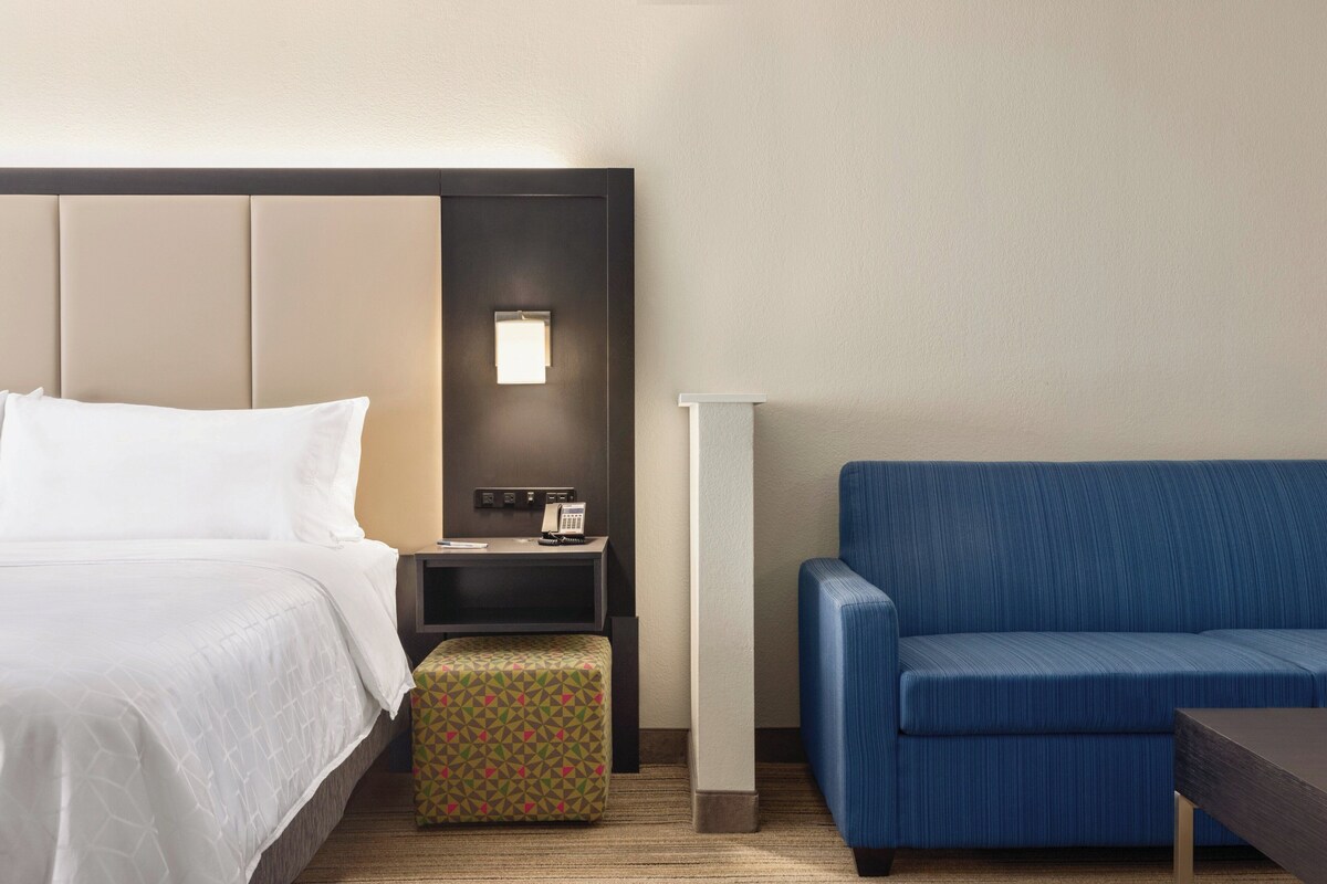 Ein Hotelzimmer mit einem Bett, einem kleinen Schreibtisch mit Telefon, einem blauen Sofa und einem gemusterten Hocker.