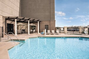 A swimming pool with lounge chairs and umbrellas, surrounded by a building with a stone facade and a covered patio area.