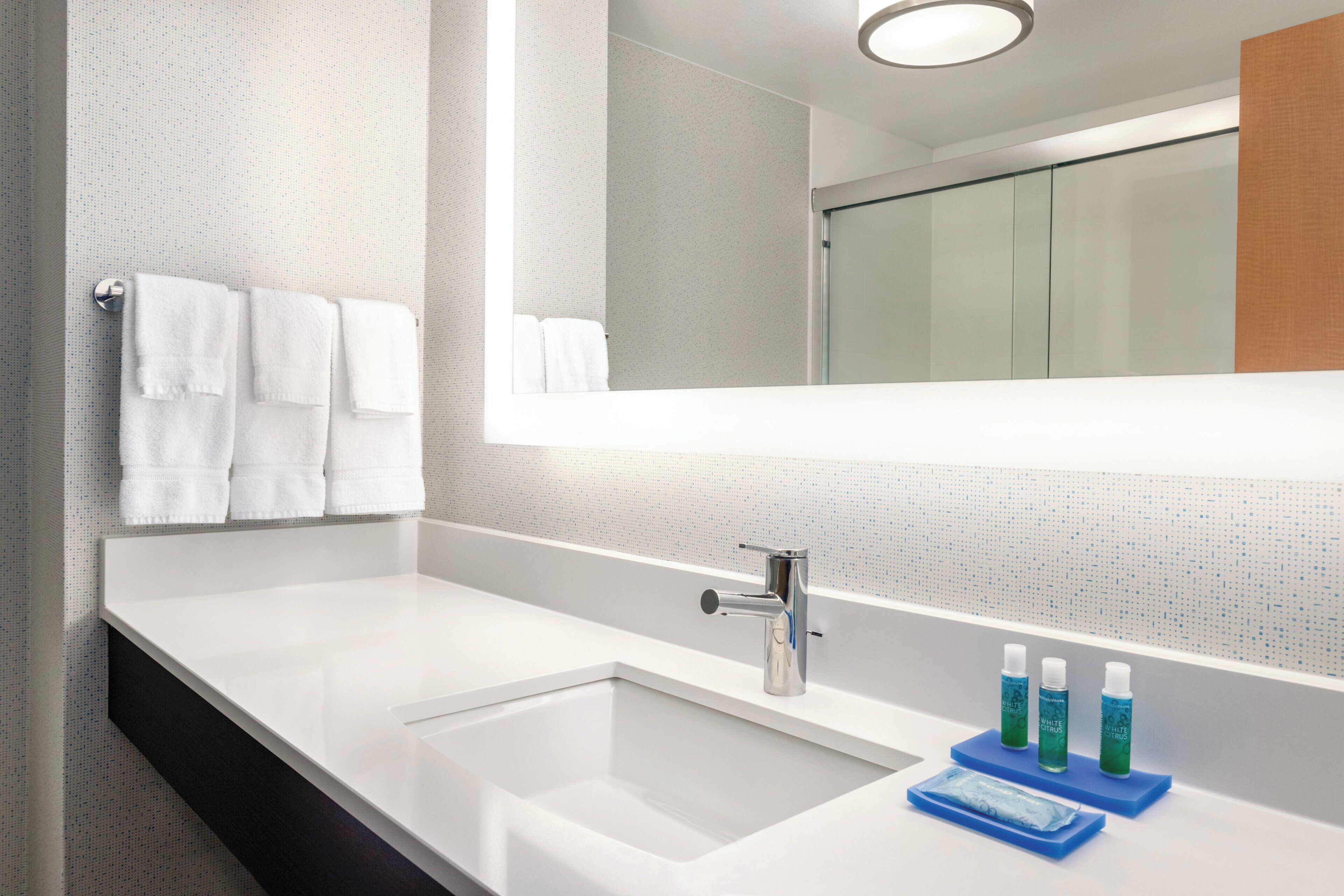 A modern bathroom with a large mirror, white sink, and three bottles of liquid soap on a blue soap dish.