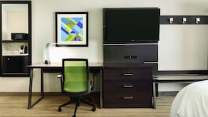 Ein Hotelzimmer mit Schreibtisch, Stuhl, Fernseher und einem gerahmten Bild an der Wand.