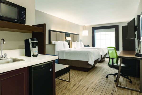 Ein Hotelzimmer mit Bett, Schreibtisch, Stuhl, Mikrowelle, Kaffeemaschine und Fernseher.