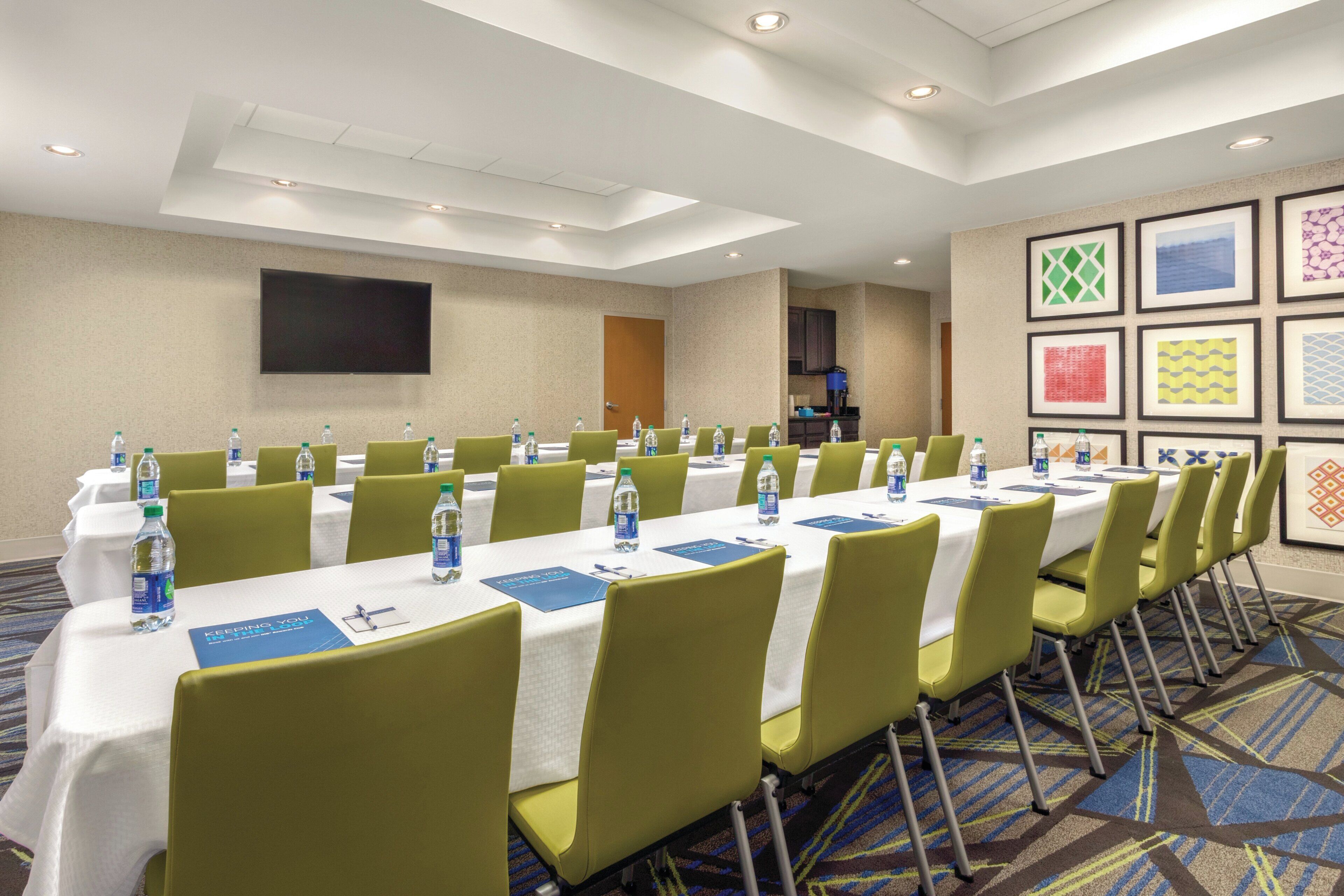A conference room with tables, chairs, water bottles, and a TV screen.